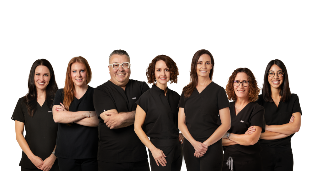 Tulsa OB-GYN physicians in black scrubs pose for a group photo in front of a white backdrop